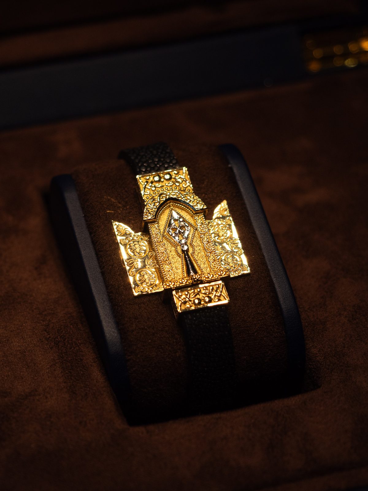 A gold bracelet with an arched ornamental centre on a black strap
