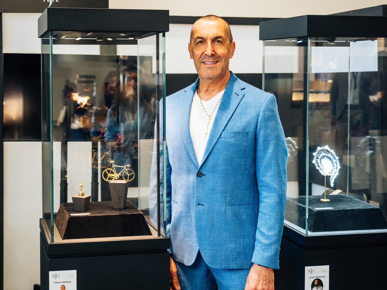 A man in a light blue suit standing between glass cases of jewellery at an exhibition