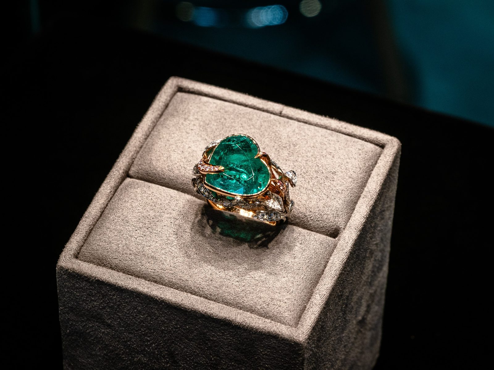 A gold ring with a large green gemstone on a grey display stand