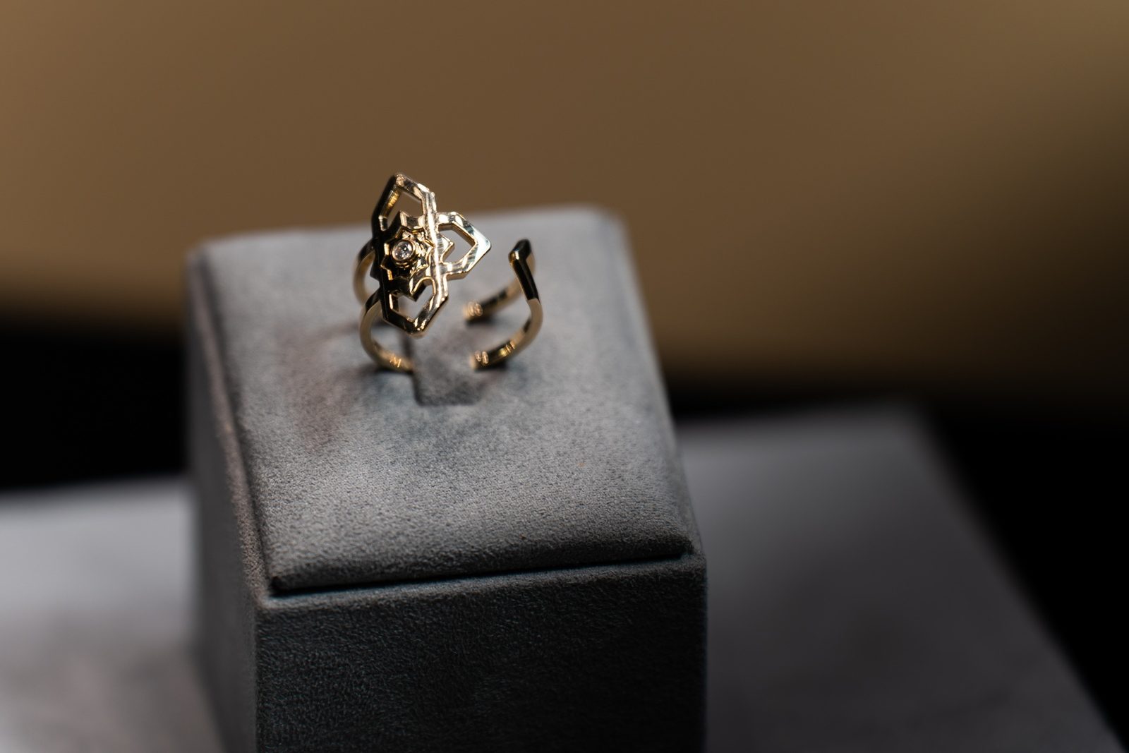 An open gold ring with a geometric setting on a grey display stand